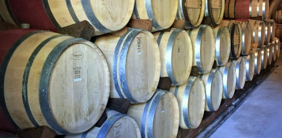 A row of wooden wine barrels stacked against a wall in a cellar.