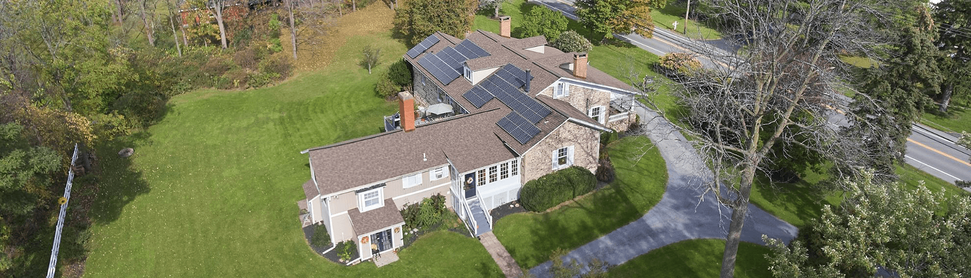 Aerial view of a house with solar panels surrounded by greenery and a winding driveway.